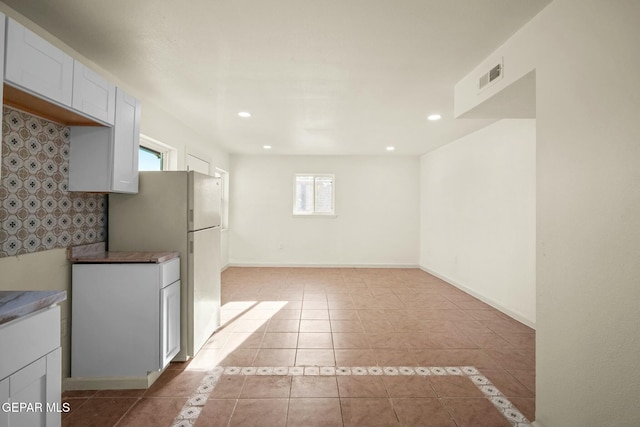 kitchen featuring white refrigerator, light tile patterned floors, and white cabinets