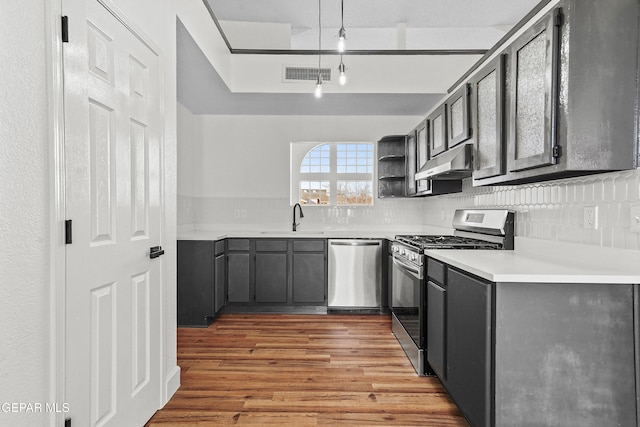 kitchen featuring sink, hanging light fixtures, stainless steel appliances, light hardwood / wood-style floors, and backsplash