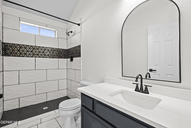 bathroom with a tile shower, vanity, and toilet