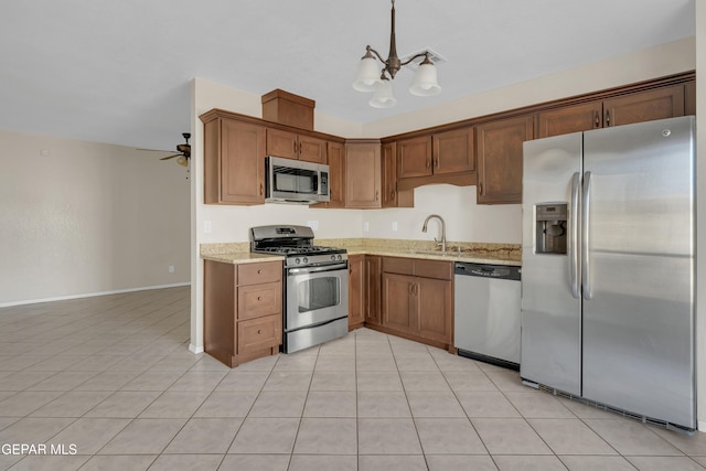 kitchen with appliances with stainless steel finishes, ceiling fan with notable chandelier, pendant lighting, sink, and light stone countertops