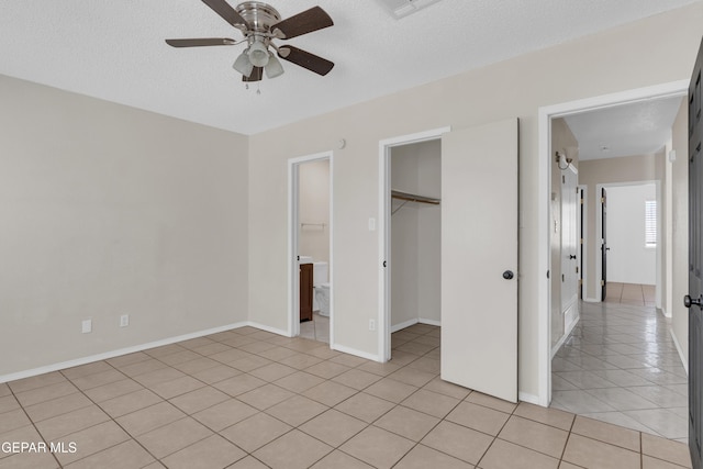 unfurnished bedroom with a walk in closet, light tile patterned floors, ceiling fan, a textured ceiling, and a closet