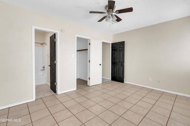 unfurnished bedroom with light tile patterned floors, ceiling fan, a textured ceiling, a spacious closet, and a closet