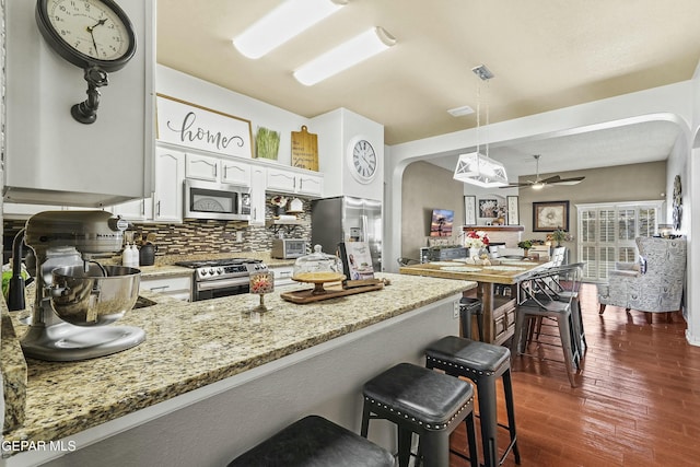 kitchen with appliances with stainless steel finishes, white cabinetry, a kitchen breakfast bar, hanging light fixtures, and kitchen peninsula