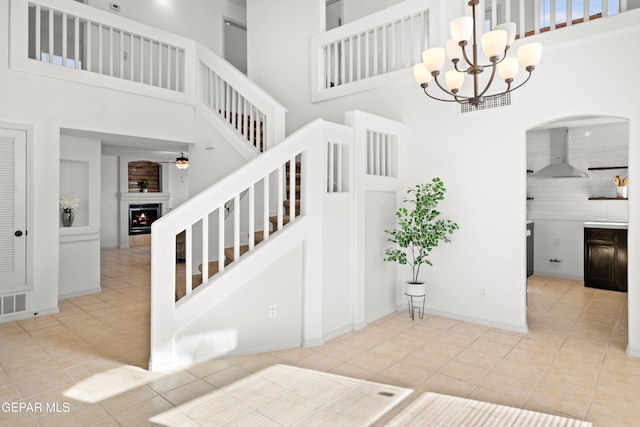 stairs with a towering ceiling, tile patterned floors, and ceiling fan with notable chandelier