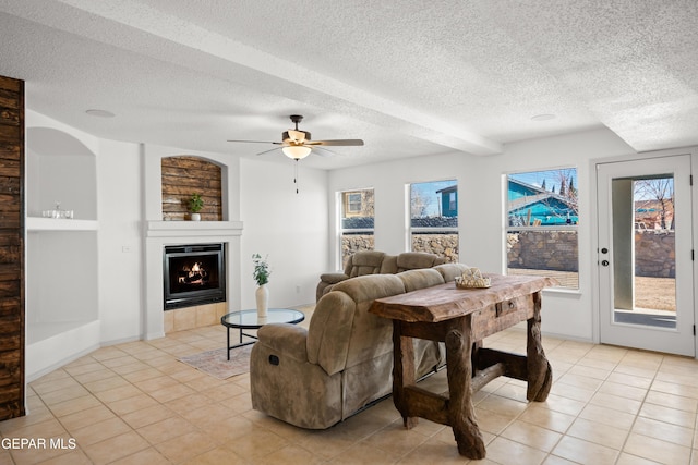 living room featuring ceiling fan, a fireplace, a textured ceiling, and light tile patterned flooring