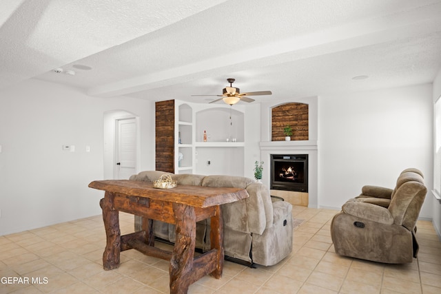 living room with light tile patterned flooring, beamed ceiling, ceiling fan, a textured ceiling, and built in shelves