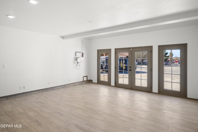 empty room with light hardwood / wood-style flooring, beam ceiling, and french doors