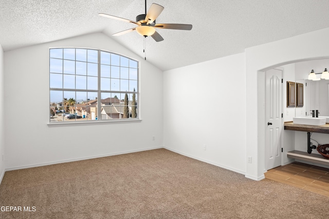 unfurnished room with sink, vaulted ceiling, a textured ceiling, carpet floors, and ceiling fan