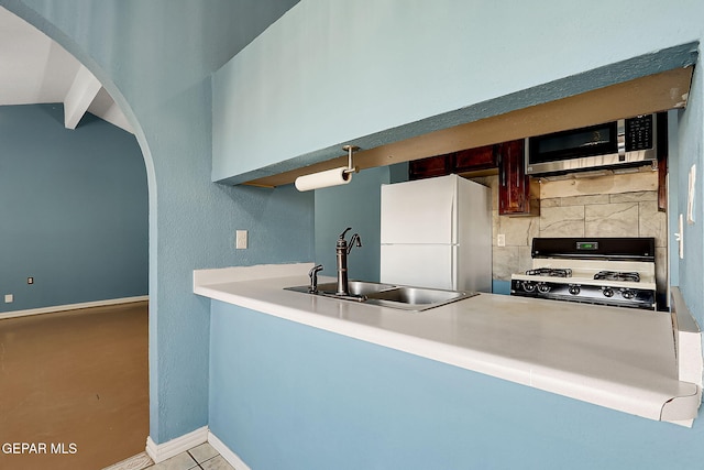 kitchen with sink, range with gas cooktop, tasteful backsplash, white refrigerator, and kitchen peninsula