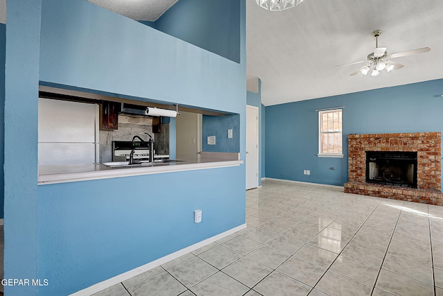 kitchen with sink, a textured ceiling, a brick fireplace, light tile patterned floors, and ceiling fan