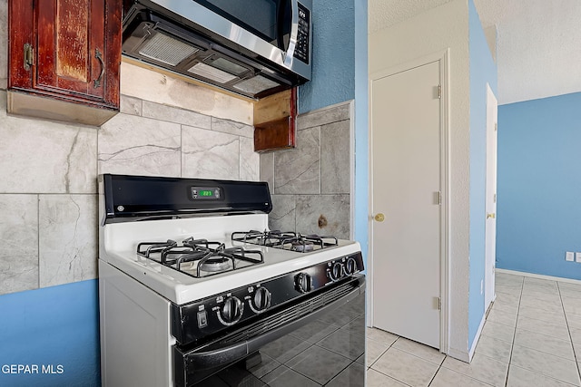 kitchen featuring white range with gas cooktop, light tile patterned floors, a textured ceiling, and tile walls