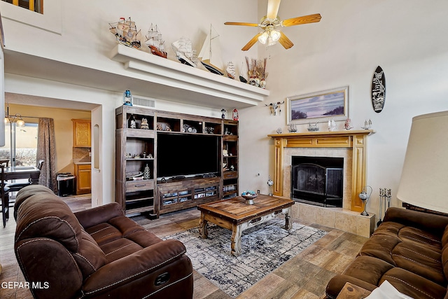 living room with ceiling fan, a towering ceiling, hardwood / wood-style floors, and a tile fireplace