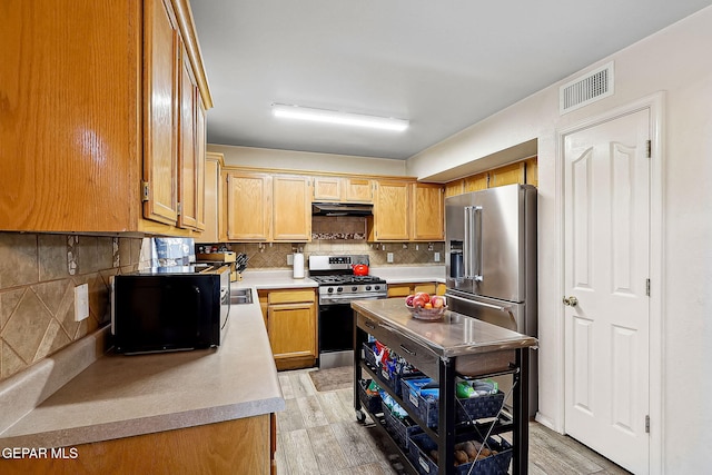 kitchen featuring light brown cabinetry, backsplash, light wood-type flooring, and appliances with stainless steel finishes