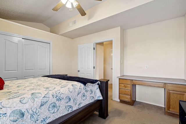 bedroom featuring ceiling fan, built in desk, vaulted ceiling, light colored carpet, and a closet