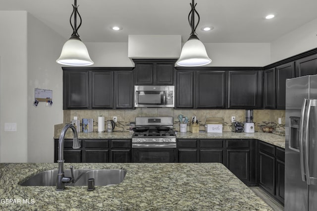 kitchen with light stone countertops, appliances with stainless steel finishes, sink, and decorative light fixtures