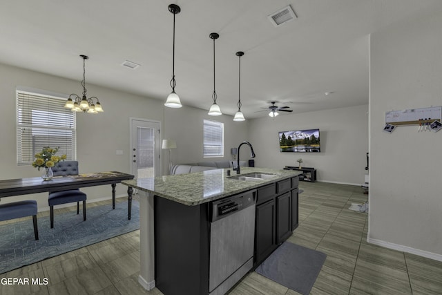 kitchen with pendant lighting, sink, a kitchen island with sink, light stone countertops, and stainless steel dishwasher