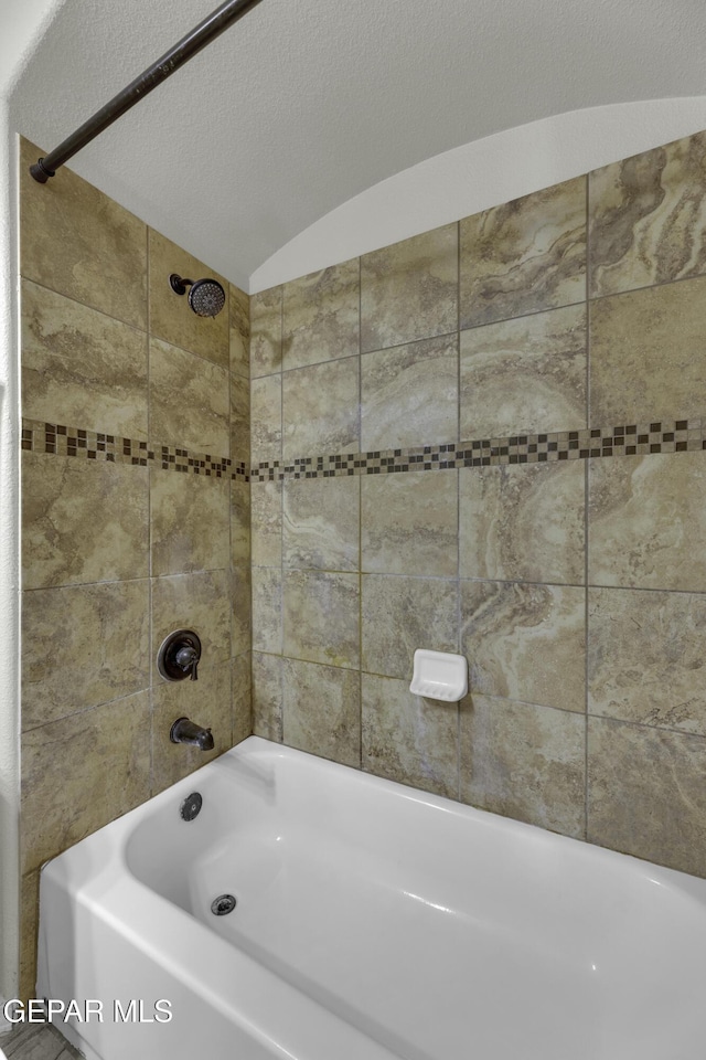 bathroom with a textured ceiling, vaulted ceiling, and tiled shower / bath