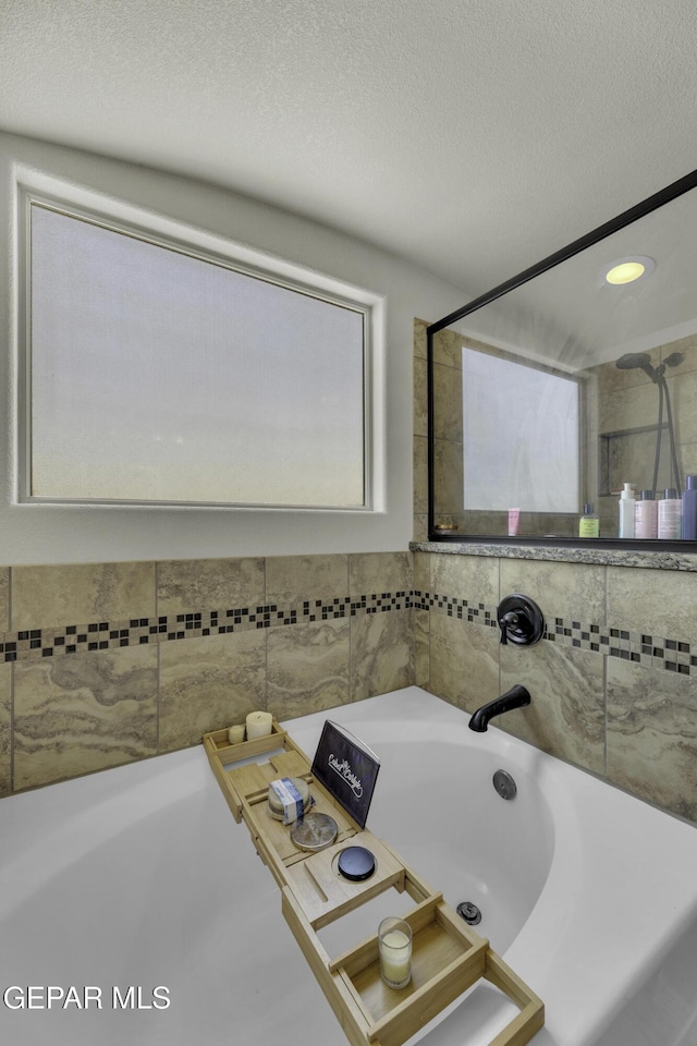 bathroom with a textured ceiling and tiled shower / bath