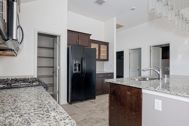 kitchen with light stone counters, sink, dark brown cabinets, and black fridge