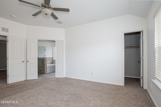 unfurnished bedroom with vaulted ceiling, ensuite bathroom, a walk in closet, light colored carpet, and a closet