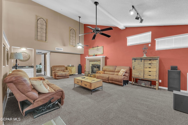 carpeted living room featuring ceiling fan, high vaulted ceiling, track lighting, a textured ceiling, and a stone fireplace