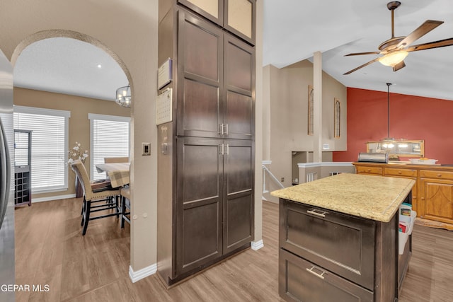 kitchen with vaulted ceiling, hanging light fixtures, a center island, dark brown cabinetry, and light hardwood / wood-style flooring