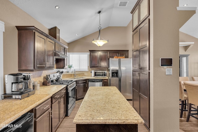 kitchen featuring lofted ceiling, sink, decorative light fixtures, appliances with stainless steel finishes, and a kitchen island