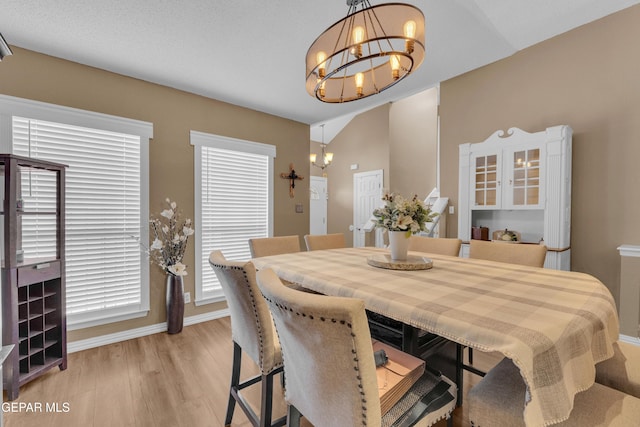 dining area with lofted ceiling, a notable chandelier, and light hardwood / wood-style flooring