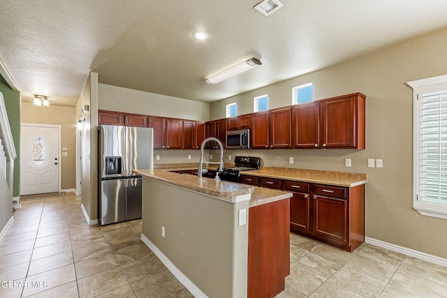 kitchen with light stone countertops, appliances with stainless steel finishes, a healthy amount of sunlight, and a center island with sink