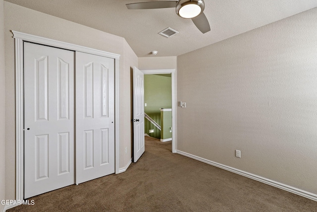 unfurnished bedroom featuring dark colored carpet, a textured ceiling, ceiling fan, and a closet