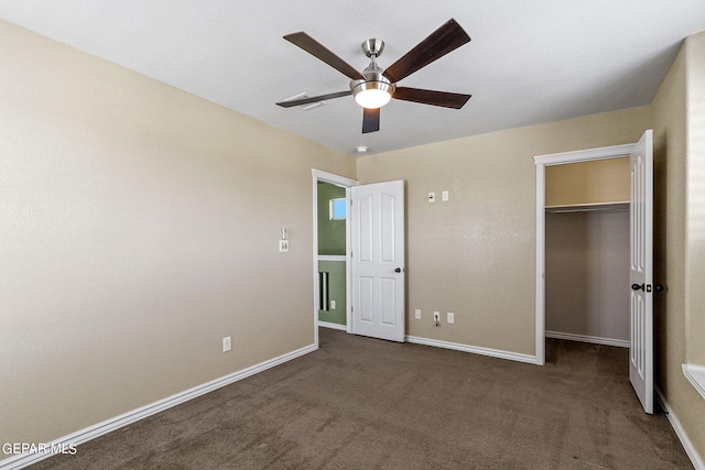 unfurnished bedroom featuring dark colored carpet, a walk in closet, ceiling fan, and a closet