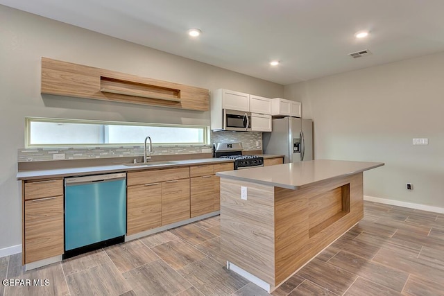 kitchen with sink, backsplash, stainless steel appliances, white cabinets, and a kitchen island