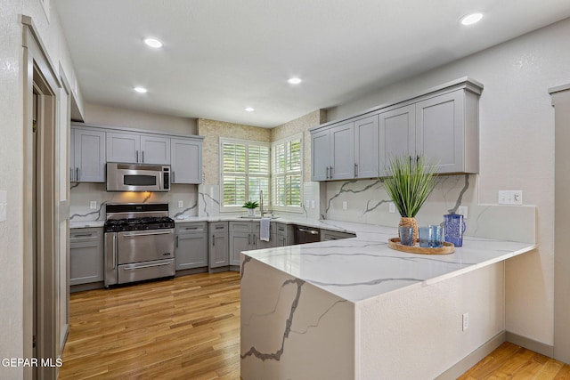 909 Singing Hills Dr, El Paso, TX 79912 - kitchen featuring stainless steel appliances, gray cabinets, a peninsula, a sink, and light wood finished floors
