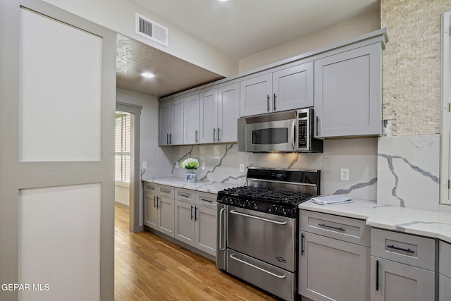 909 Singing Hills Dr, El Paso, TX 79912 - kitchen with stainless steel appliances, gray cabinetry, light wood-style flooring, and light stone countertops
