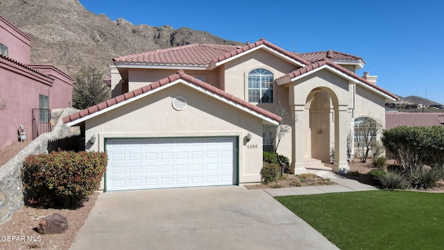 mediterranean / spanish house with stucco siding, a tile roof, a garage, and concrete driveway