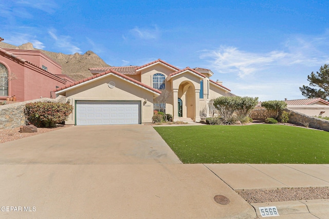 mediterranean / spanish home with driveway, stucco siding, a front lawn, a tiled roof, and a garage
