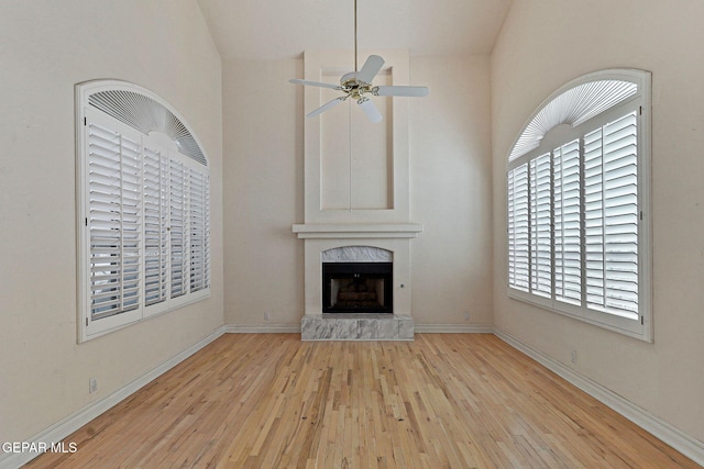 unfurnished living room featuring high vaulted ceiling, baseboards, a fireplace, wood finished floors, and ceiling fan