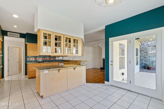 kitchen with light tile patterned floors, glass insert cabinets, a breakfast bar area, and a peninsula