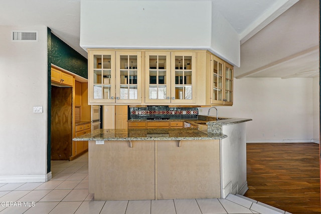 kitchen with a breakfast bar area, dark stone counters, a sink, visible vents, and a peninsula