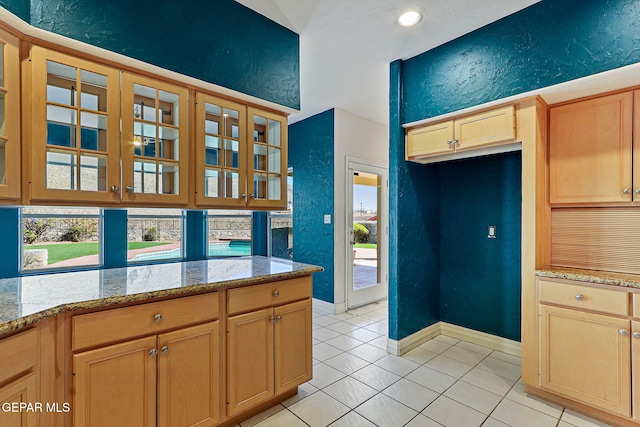 kitchen with glass insert cabinets, light stone countertops, and a textured wall