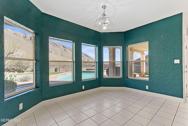 empty room with baseboards, tile patterned flooring, a mountain view, and a chandelier