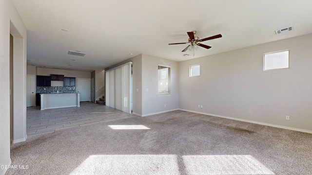 unfurnished living room featuring ceiling fan, light colored carpet, and a healthy amount of sunlight