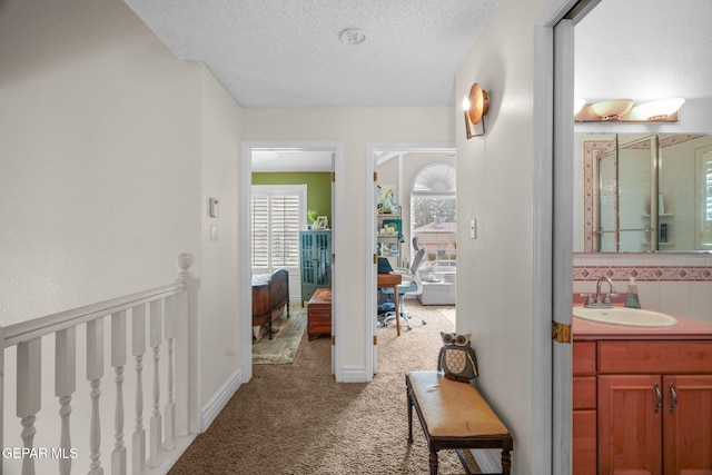 corridor with sink, carpet floors, and a textured ceiling