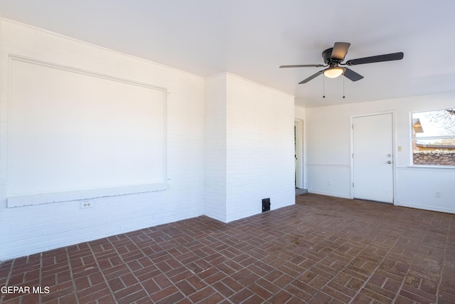 spare room with ceiling fan and brick wall