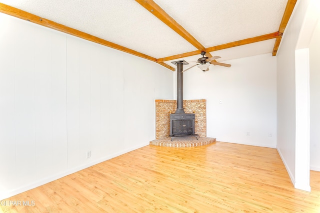 unfurnished living room with ceiling fan, beam ceiling, wood-type flooring, a textured ceiling, and a wood stove