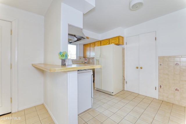 kitchen featuring tile walls, light tile patterned floors, white refrigerator with ice dispenser, kitchen peninsula, and range hood