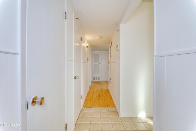 hall with light tile patterned flooring and a textured ceiling