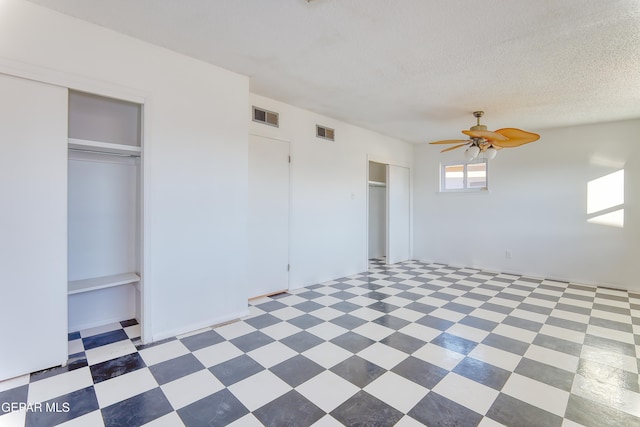 unfurnished bedroom with ceiling fan, a textured ceiling, and two closets