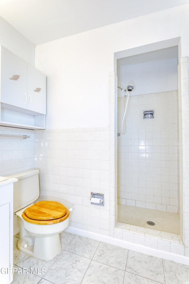 bathroom featuring vanity, toilet, tile walls, and a tile shower