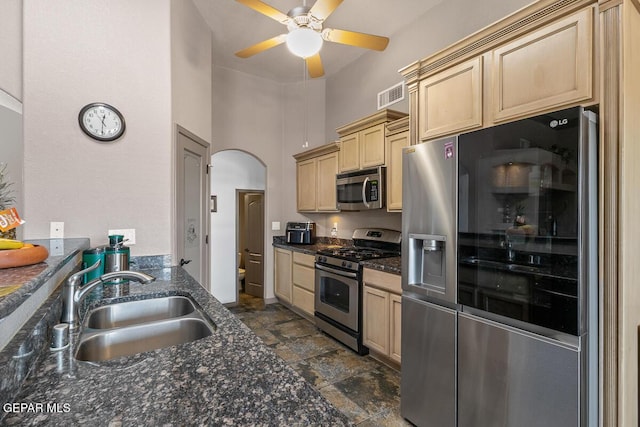 kitchen with sink, dark stone countertops, ceiling fan, stainless steel appliances, and light brown cabinets